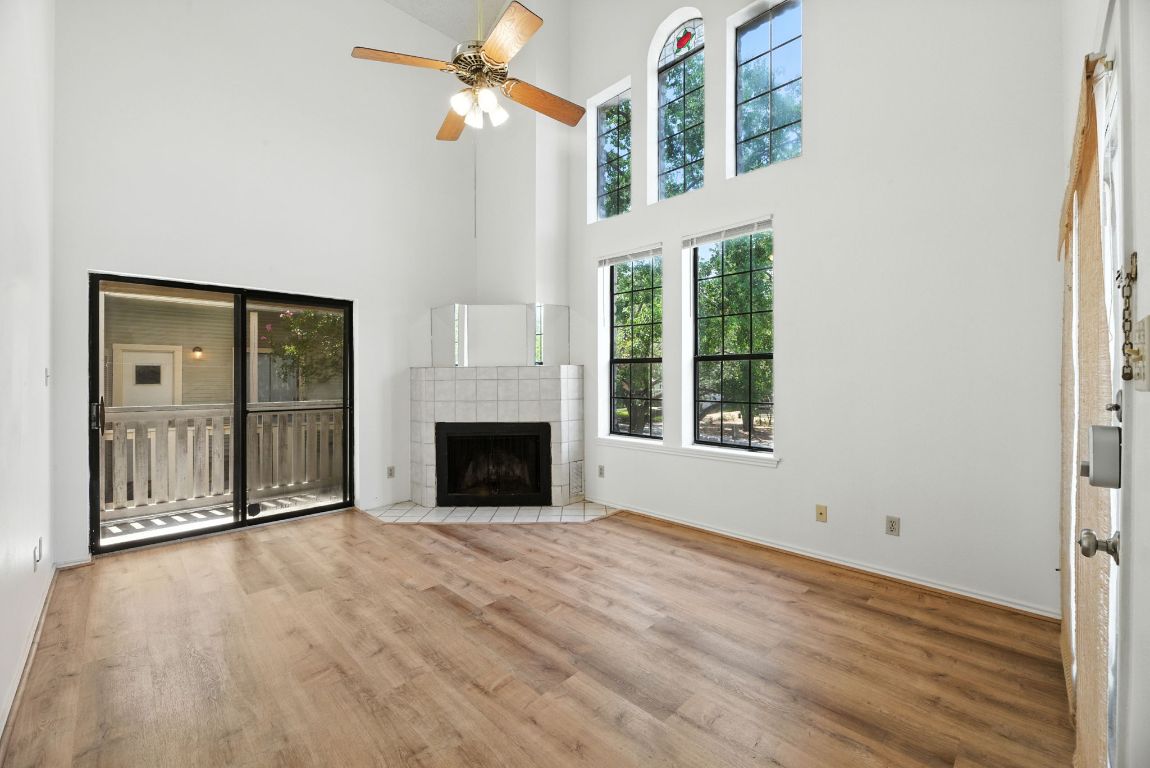 4409 Speedway, Unit 201 Austin, TX 78751 - Photo 3 of 16 Unfurnished living room featuring a fireplace, wood finished floors, a towering ceiling, healthy amount of natural light, and a ceiling fan
