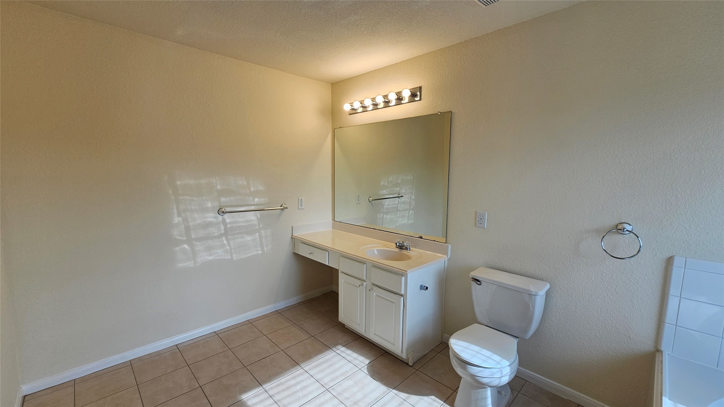7918 Barnes Ridge Lane Houston, TX 77072 - Photo 16 of 34 This bathroom features a spacious layout with neutral tile flooring. It includes a single vanity with a large mirror, ample counter space, and a well-lit fixture above. The room also has a toilet and a towel ring, with a towel bar on the opposite wall, creating a functional, bright space.