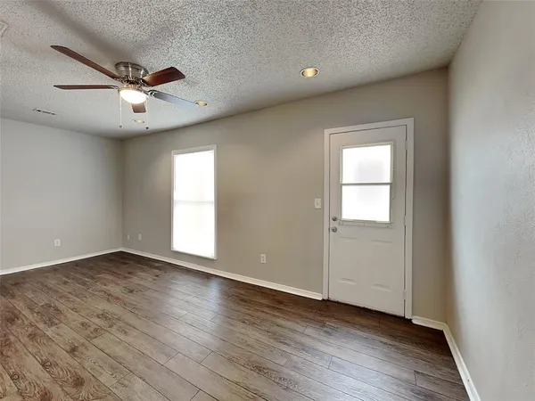 an empty room with wooden floor a ceiling fan and windows