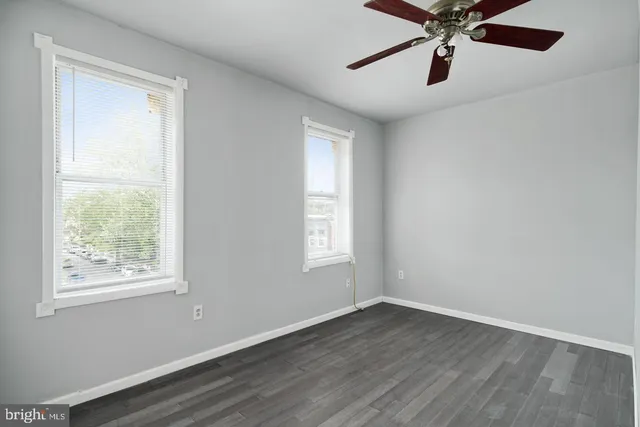 an empty room with wooden floor fan and windows