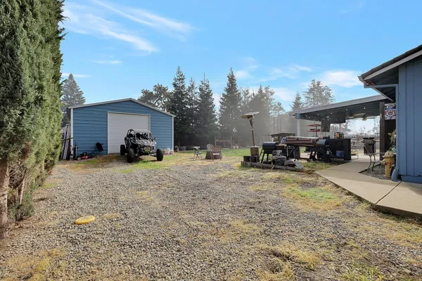 a view of a house with a barbeque and large trees