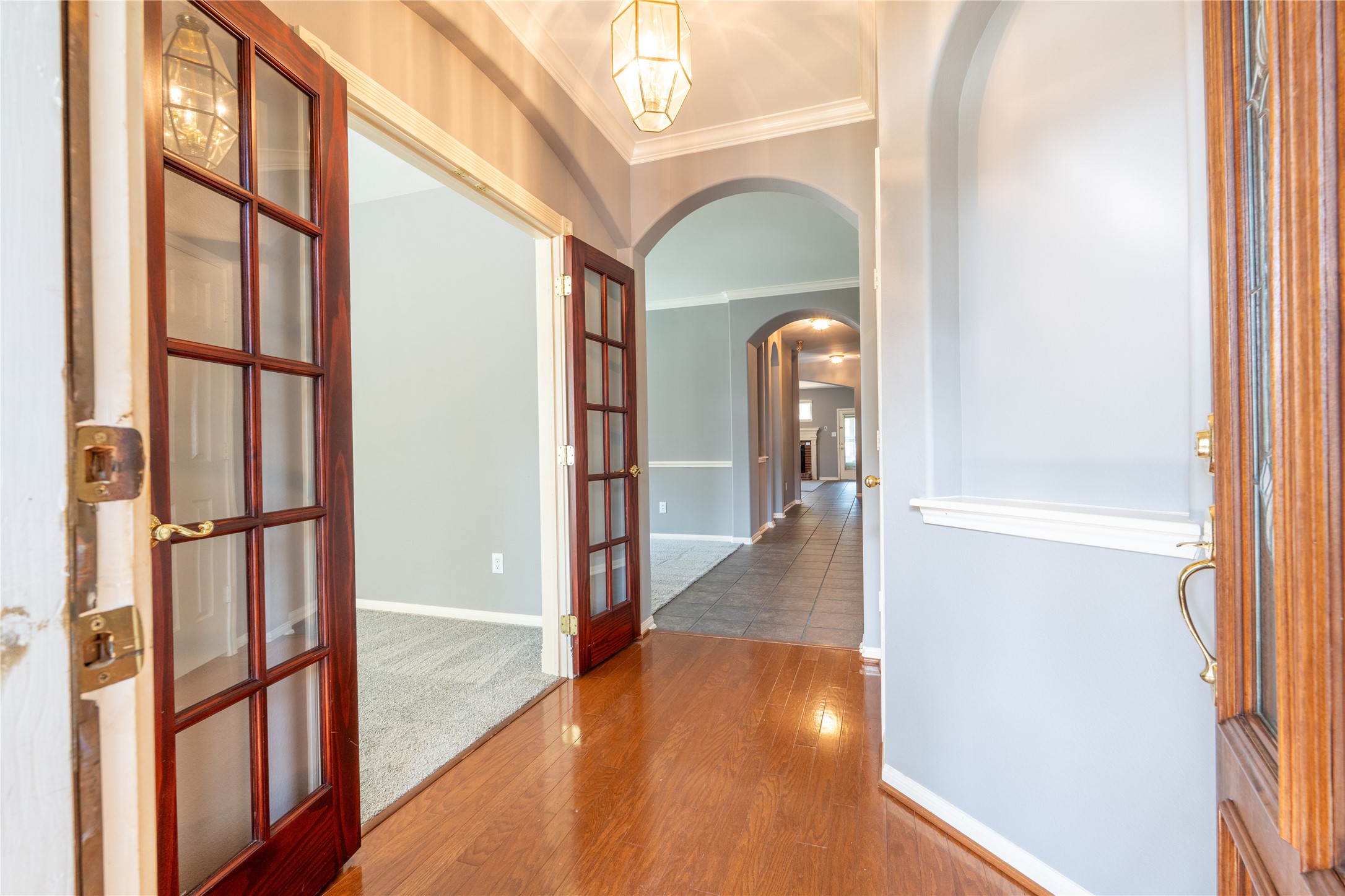 10619 Crownsedge Drive Spring, TX 77379 - Photo 4 of 38 The inviting entryway features warm hardwood flooring and elegant French doors leading to the office/flex fourth bedroom. The hallway extends with tiled flooring, arched doorways, and soft lighting, providing a welcoming feel.