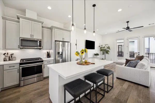 a living room with stainless steel appliances kitchen island granite countertop a stove a sink a dining table and chairs with wooden floor