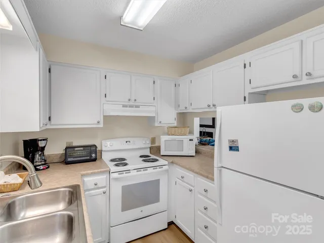 a white kitchen with sink a refrigerator and white cabinets