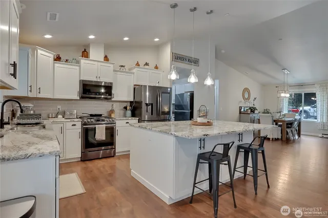 a kitchen with stainless steel appliances kitchen island granite countertop a stove a sink a refrigerator and white cabinets with wooden floor