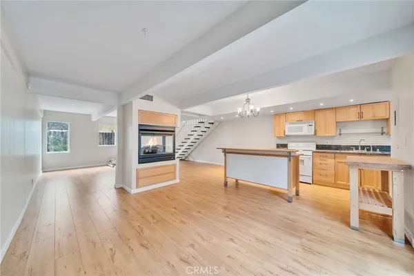 a view of an empty room and kitchen with wooden floor