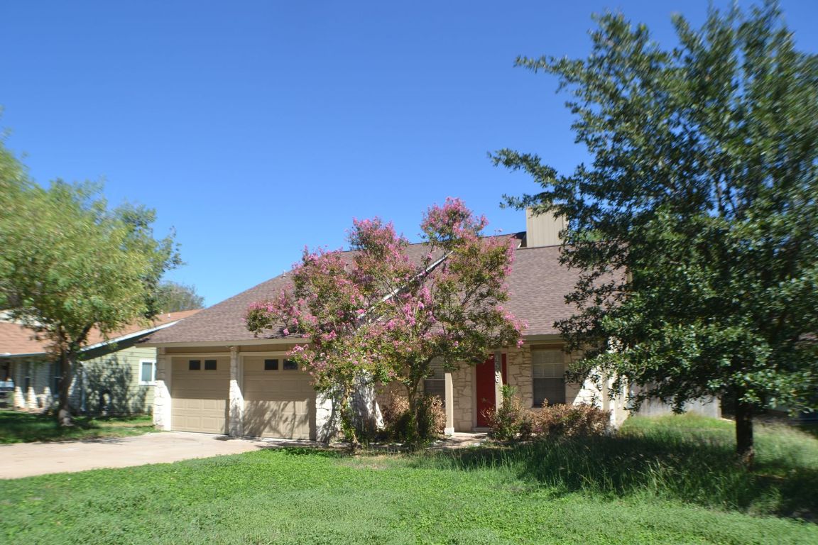 4506 Adelphi Lane Austin, TX 78727 - Photo 2 of 13 View of property hidden behind natural elements featuring stone siding, concrete driveway, a front yard, roof with shingles, and an attached garage