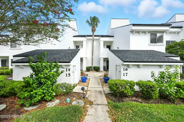 a view of a white house with large windows and a yard with plants