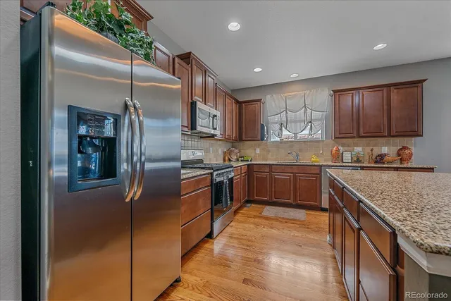 a kitchen with stainless steel appliances granite countertop a refrigerator a sink a stove and a oven