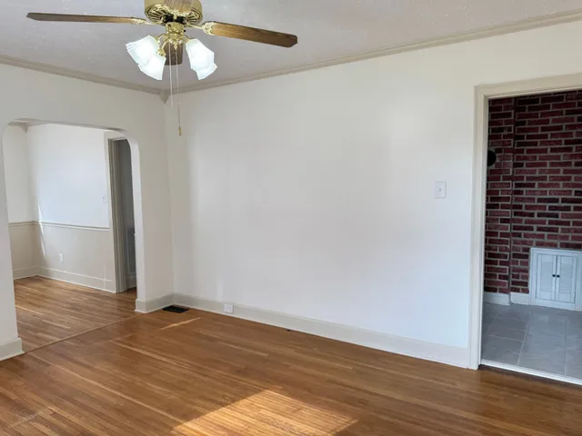 a view of an empty room with wooden floor and a chandelier fan