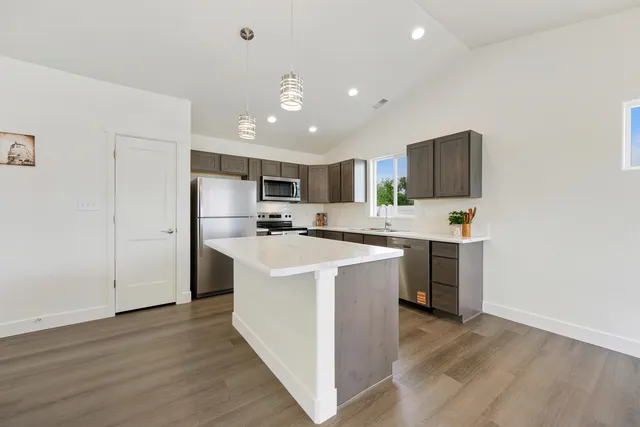 a kitchen with stainless steel appliances kitchen island granite countertop a stove a refrigerator a sink a oven with wooden cabinets and wooden floor