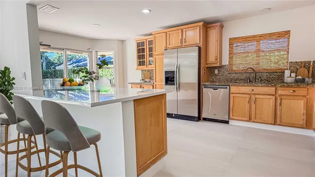 a kitchen with stainless steel appliances granite countertop a refrigerator a stove a sink and a dining table with wooden cabinet