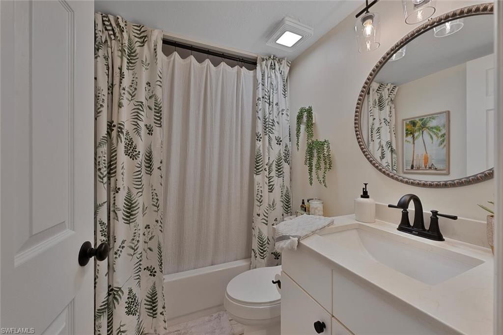 154 Cypress Way East, Unit 1102 Naples, FL 34110 - Photo 8 of 12 a bathroom with a sink a toilet a mirror and shower curtain