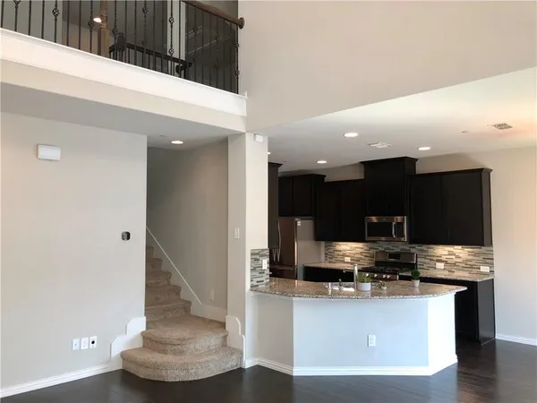 a kitchen with stainless steel appliances kitchen island granite countertop a refrigerator a stove a microwave and white cabinets with wooden floor