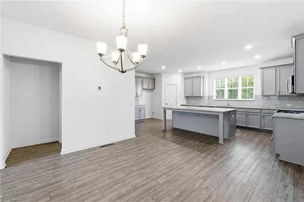 a large kitchen with kitchen island a stove a sink dishwasher a refrigerator and white cabinets with wooden floor