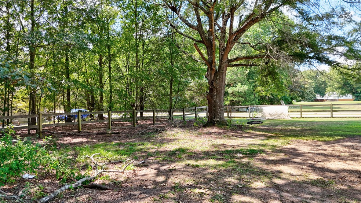 247 Clardy Road Pelzer, SC 29669 - Photo 3 of 34 Mature trees shade a spacious lawn enclosed by classic wooden fencing.