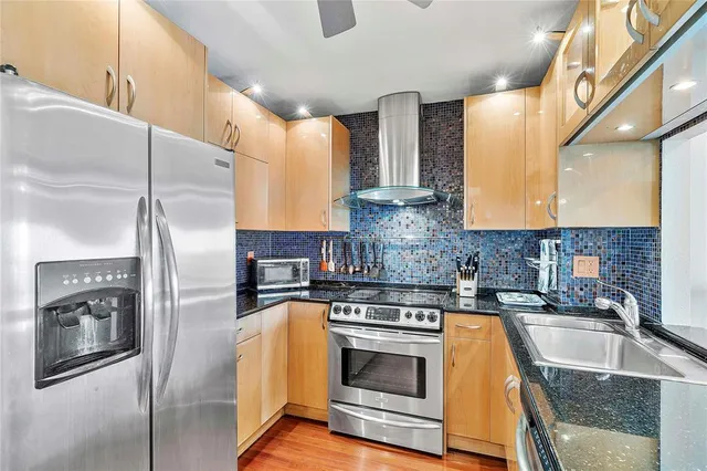 a kitchen with stainless steel appliances granite countertop a refrigerator a stove and a sink with wooden floors