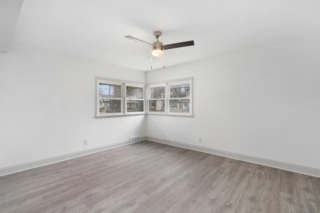 an empty room with wooden floor ceiling fan and window