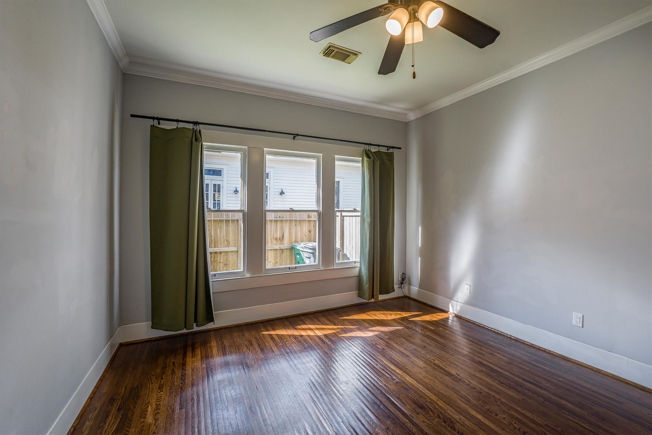 210 Tabor Street Houston, TX 77009 - Photo 10 of 18 This secondary room features hardwood floors and ample natural light from large windows with green curtains. It has a ceiling fan and neutral wall colors, creating a bright and airy atmosphere.