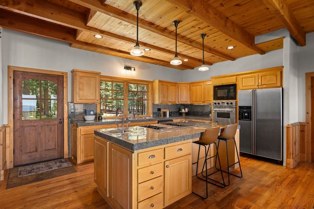 a kitchen with stainless steel appliances granite countertop a stove a refrigerator a kitchen island with chairs and wooden floor