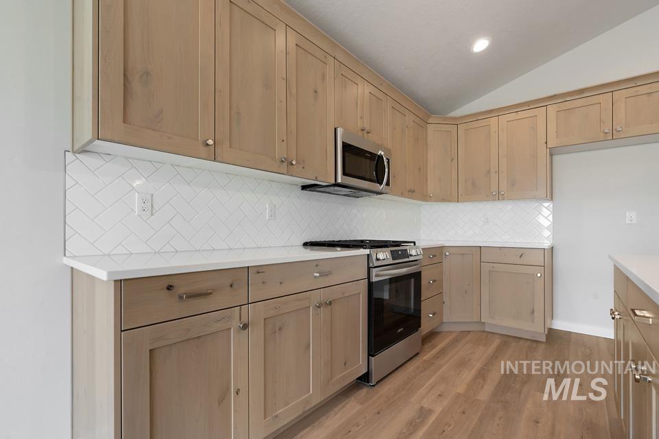 1355 Crescent Street Weiser, ID 83672 - Photo 11 of 31 Kitchen with appliances with stainless steel finishes, light brown cabinetry, vaulted ceiling, light countertops, and light wood-type flooring