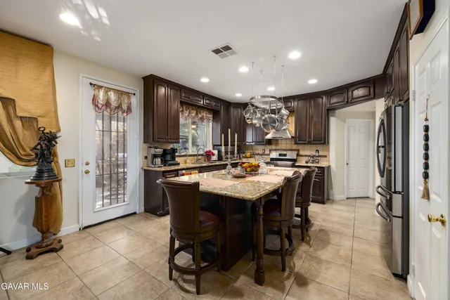 a kitchen with stainless steel appliances granite countertop a refrigerator a sink a stove and chairs