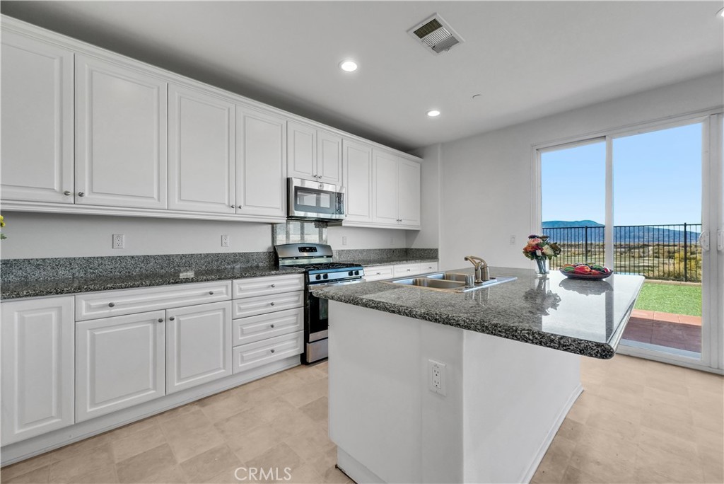 29157 Sunforest Lake Elsinore, CA 92530 - Photo 11 of 39 a kitchen with stainless steel appliances granite countertop a sink dishwasher stove and white cabinets with wooden floor