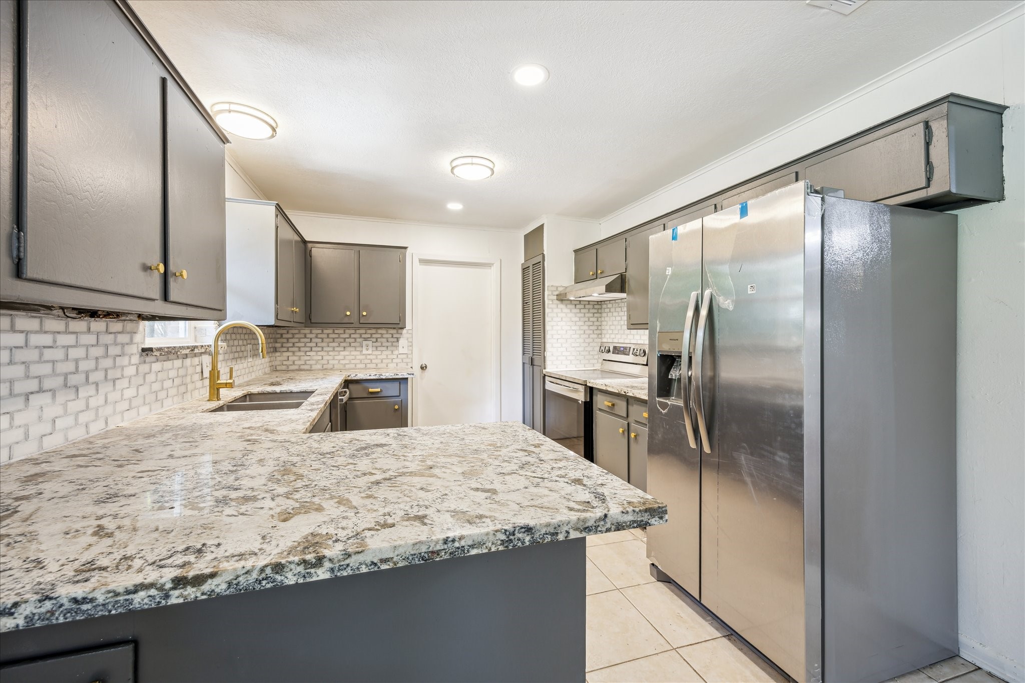 5419 Beechnut Street Houston, TX 77096 - Photo 10 of 28 Kitchen with granite counters, tile backsplash, and stainless appliances, accented by gray cabinetry and tile flooring.