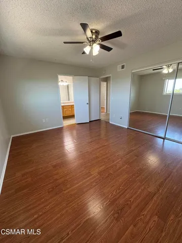 an empty room with wooden floor fan and windows