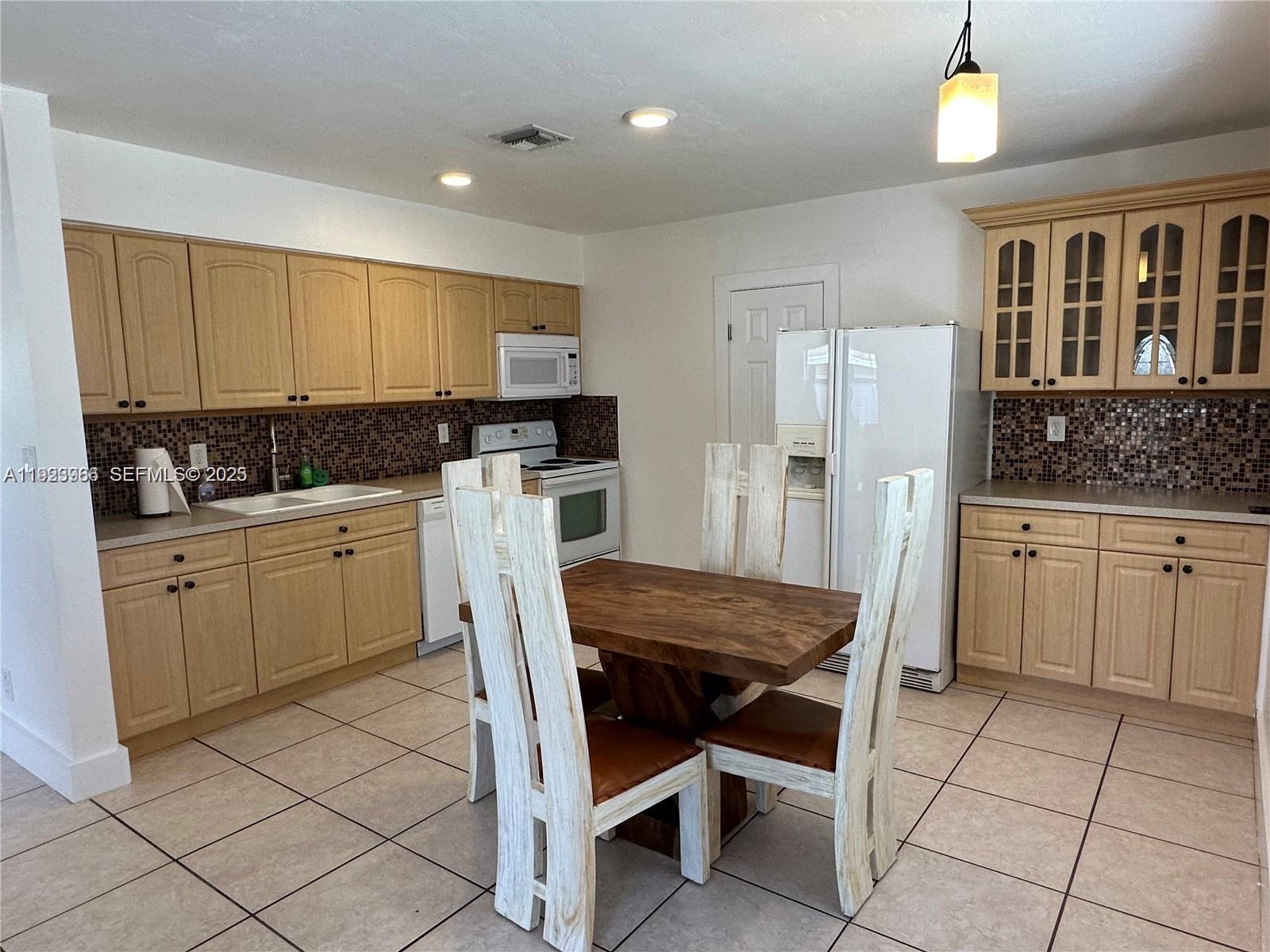 28 Southeast 4th Street Dania Beach, FL 33004 - Photo 6 of 14 a kitchen with a dining table chairs refrigerator and cabinets
