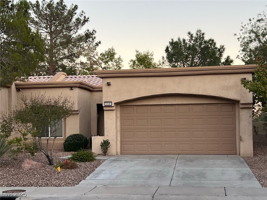 View of front of property featuring concrete driveway, stucco siding, a tile roof, and a garage