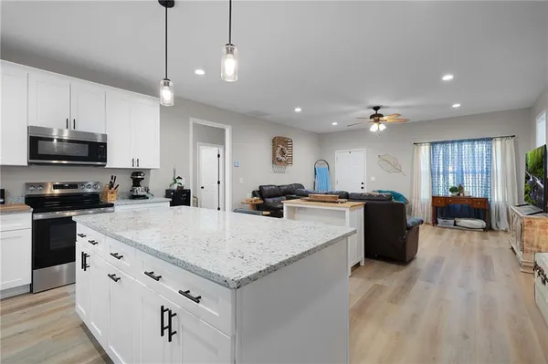 a large white kitchen with a stove a sink a kitchen island with chairs and wooden floor