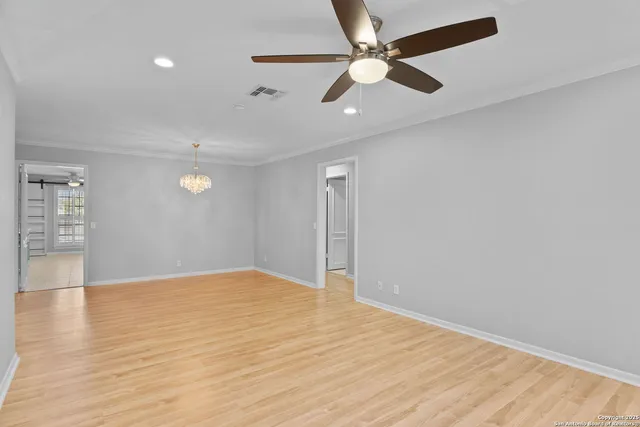 an empty room with wooden floor fan and windows