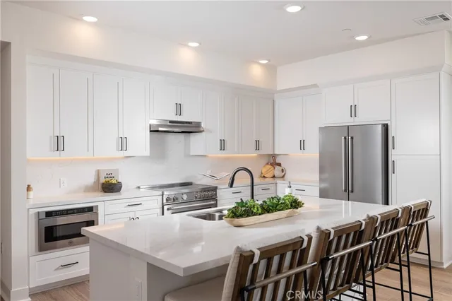 a kitchen with stainless steel appliances granite countertop a stove a refrigerator a sink a dining table and chairs