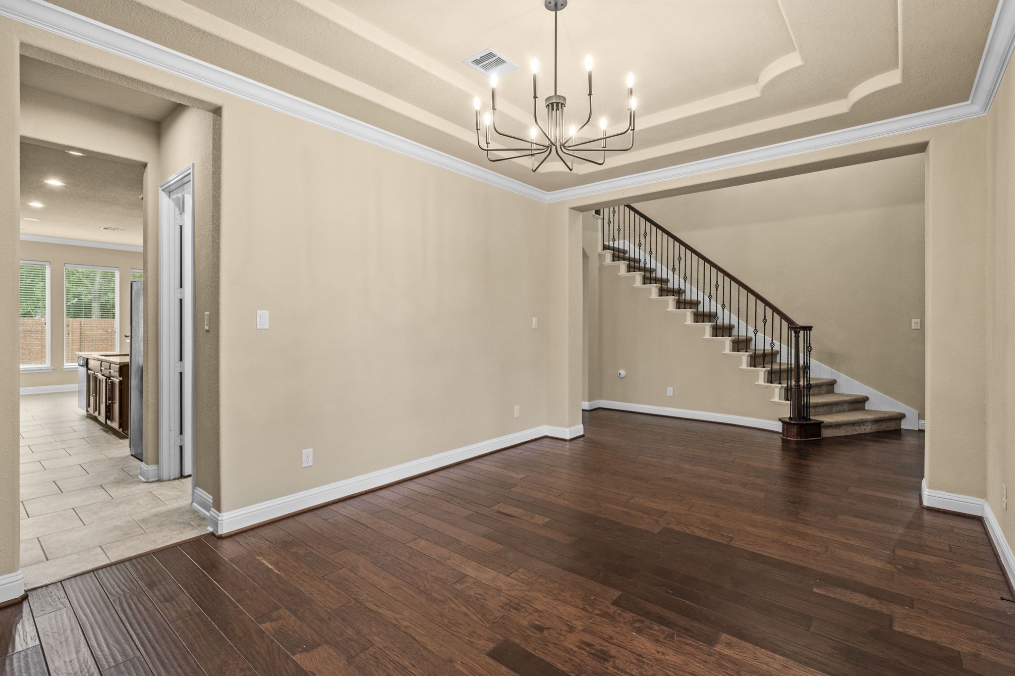 14215 Spindle Arbor Road Cypress, TX 77429 - Photo 16 of 47 This inviting home features a spacious open area with elegant hardwood floors and a stylish chandelier, leading to a staircase with wrought iron railing. The adjacent area opens to a kitchen with tile flooring and ample natural light, providing a warm and welcoming atmosphere.