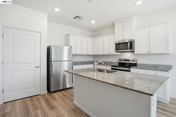 a kitchen with granite countertop a refrigerator a sink a stove a microwave and cabinets