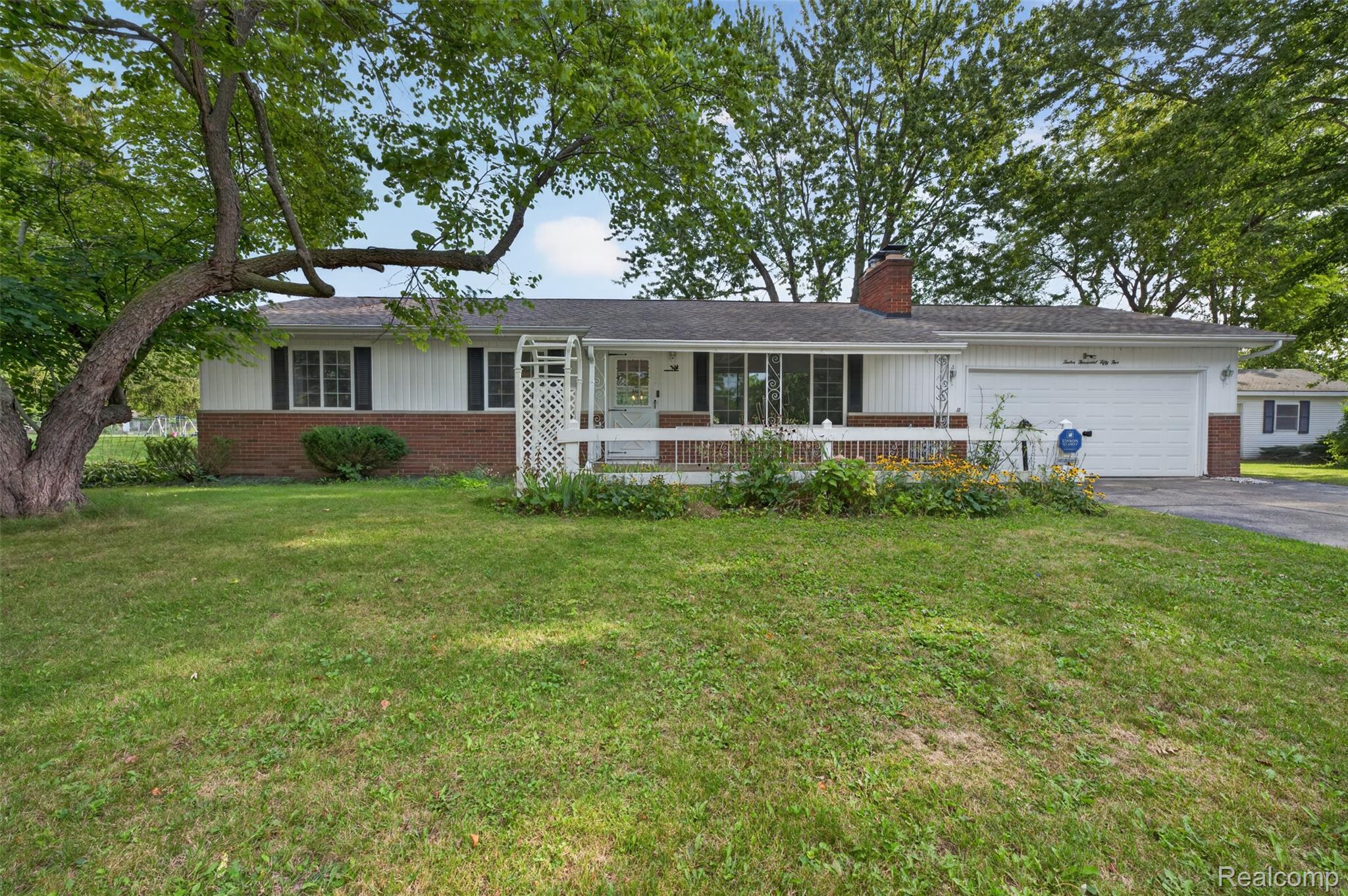 12055 West Pierson Road Flushing, MI 48433 - Photo 2 of 69 Ranch-style residence featuring a brick and white siding exterior, an attached garage, a front porch with a white railing, and a mature tree