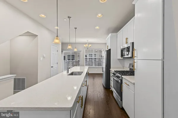 a kitchen with stainless steel appliances a stove a sink a refrigerator white cabinets and wooden floor