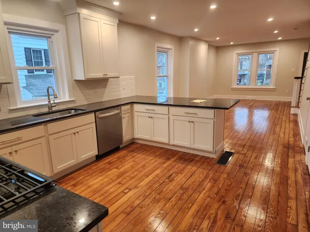 a large kitchen with stainless steel appliances granite countertop a sink dishwasher a stove and white countertops with wooden floor