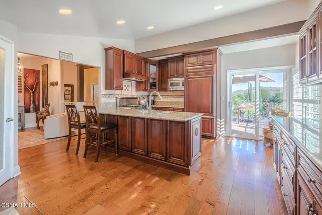 a kitchen with stainless steel appliances granite countertop a stove top oven a sink dishwasher a dining table and chairs with wooden floor