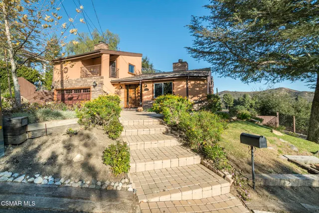 a view of a brick house with a small yard plants and a large tree