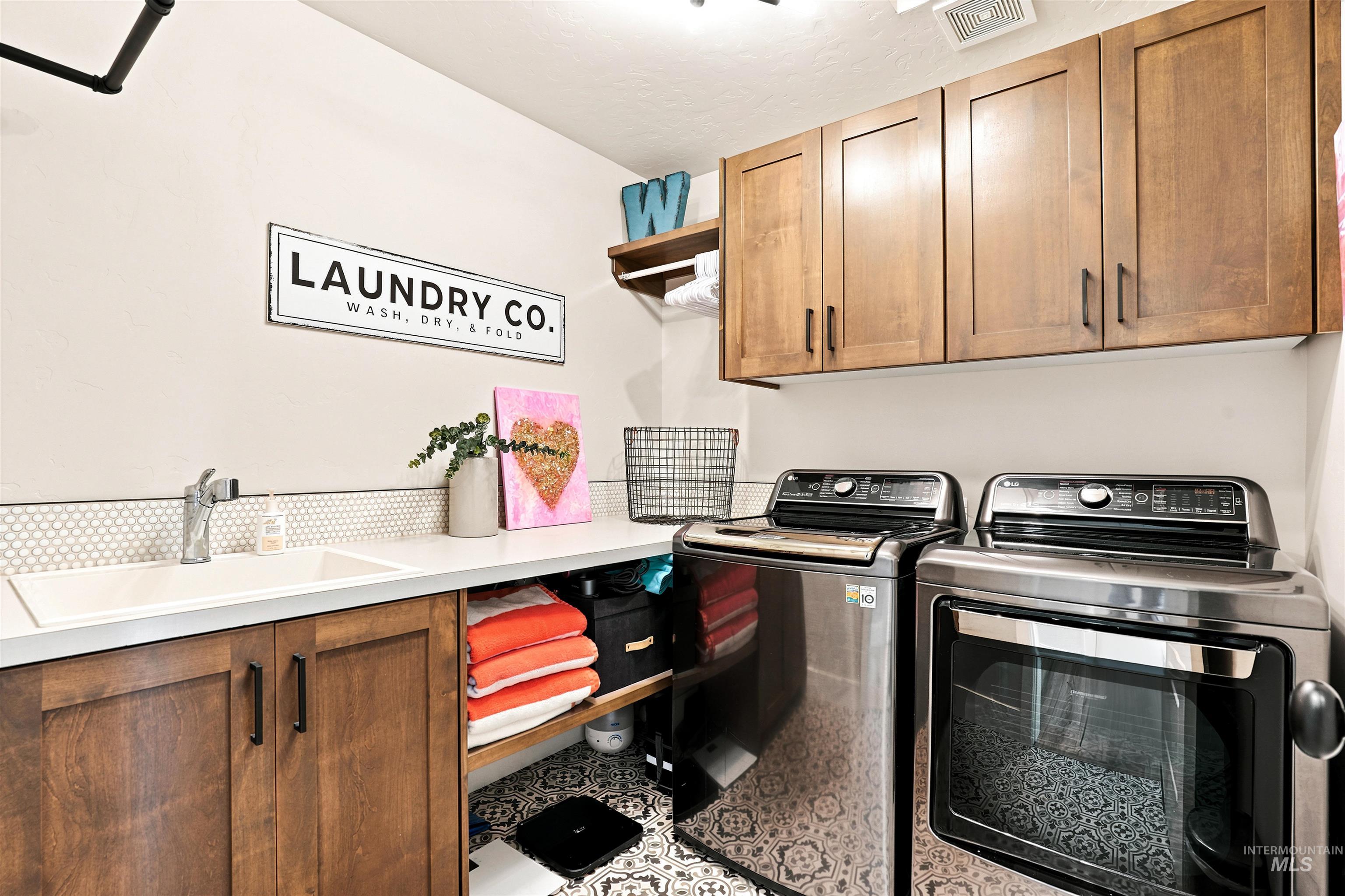 4323 West Ladle Rpds Drive Meridian, ID 83646 - Photo 37 of 49 Laundry area featuring wood cabinetry with dark hardware, a built-in sink, and patterned floor tiling