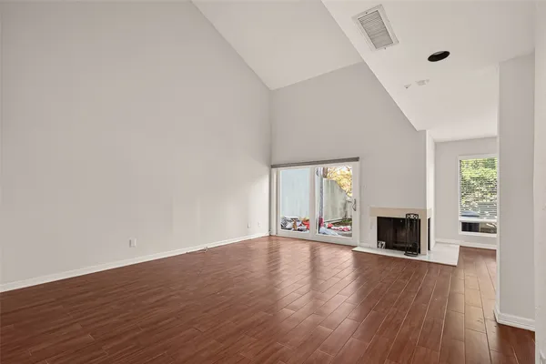 an empty room with wooden floor fireplace and windows