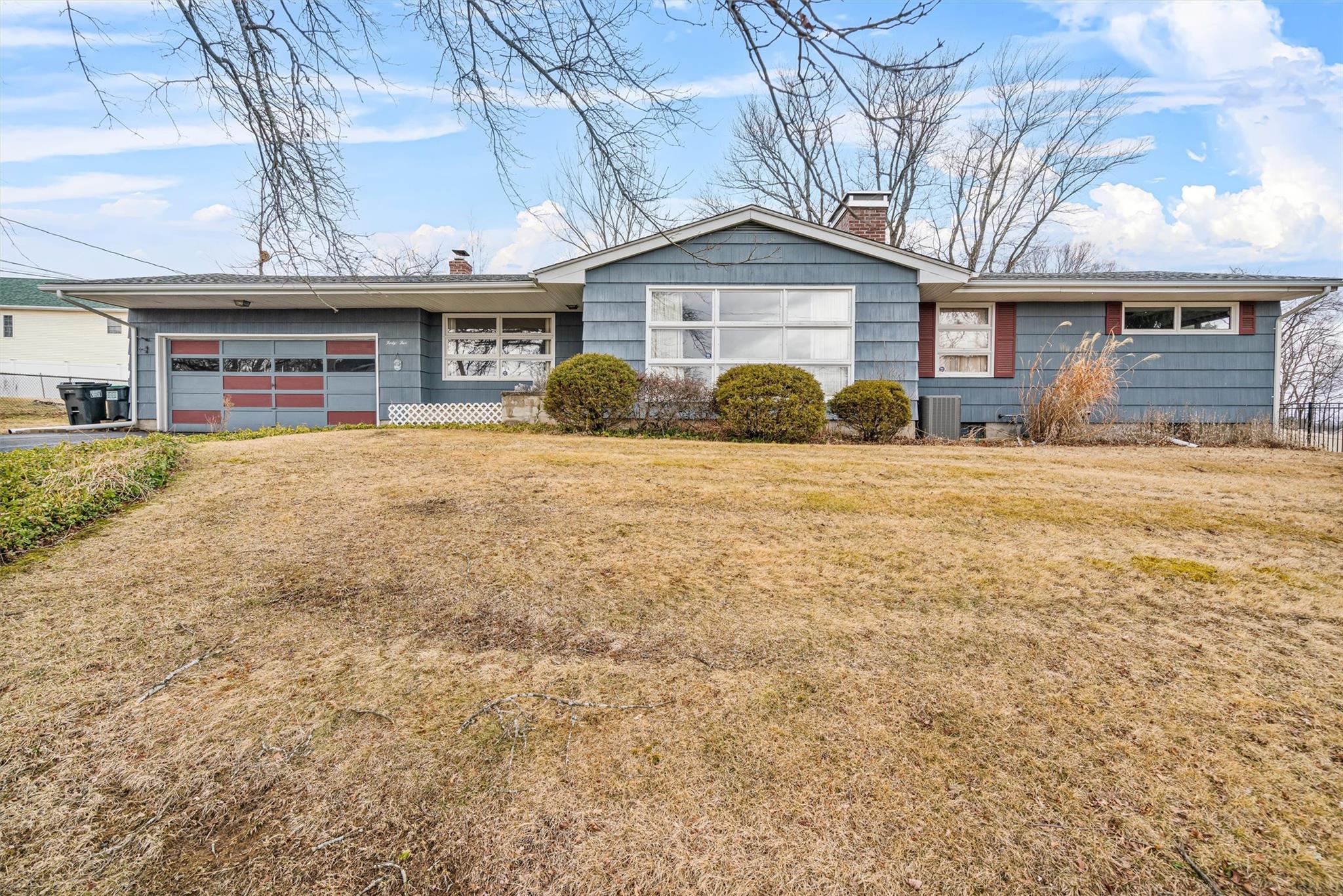 Ranch-style home featuring a chimney, central air condition unit, an attached garage, a front yard, and driveway