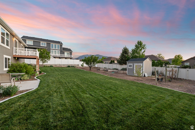 1145 North Christley Lane, Unit 48 Elk Ridge, UT 84651 - Photo 33 of 38 Expansive backyard featuring a manicured lawn, a concrete patio, a raised deck with white railings, a detached storage shed, and a white privacy fence