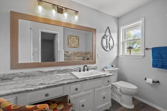 a bathroom with a granite countertop sink a toilet and a mirror