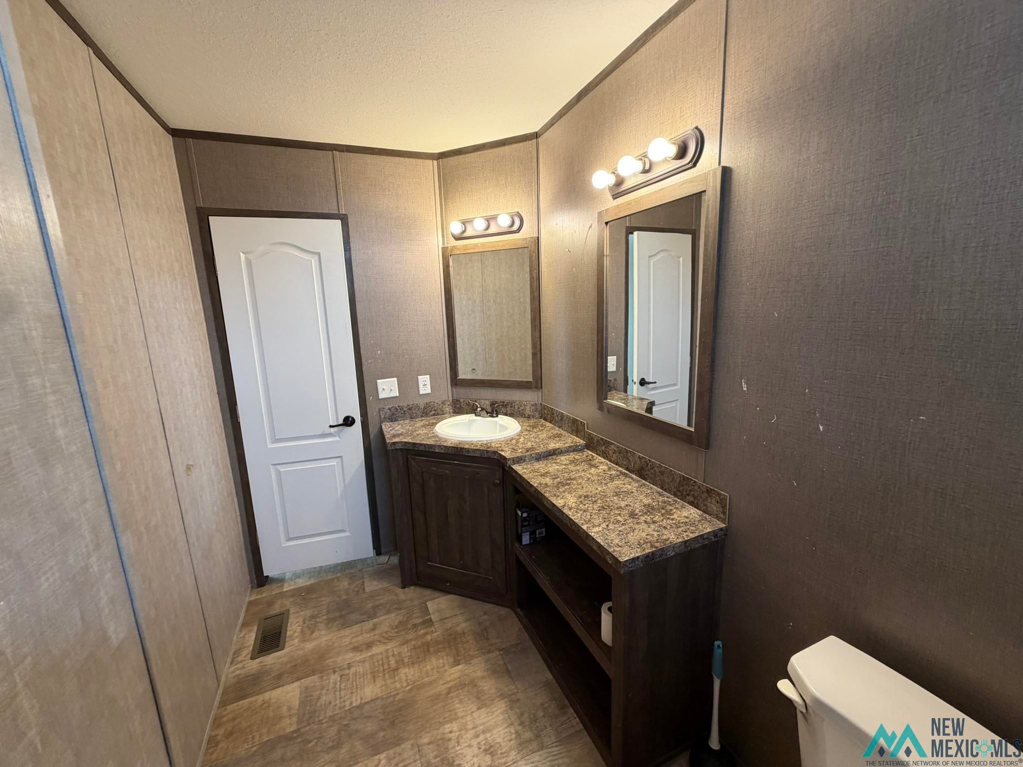 801 Riata Road Carlsbad, NM 88220 - Photo 21 of 39 Bathroom featuring a corner vanity with a built-in sink, a speckled countertop, and wood-finish cabinetry with open shelving