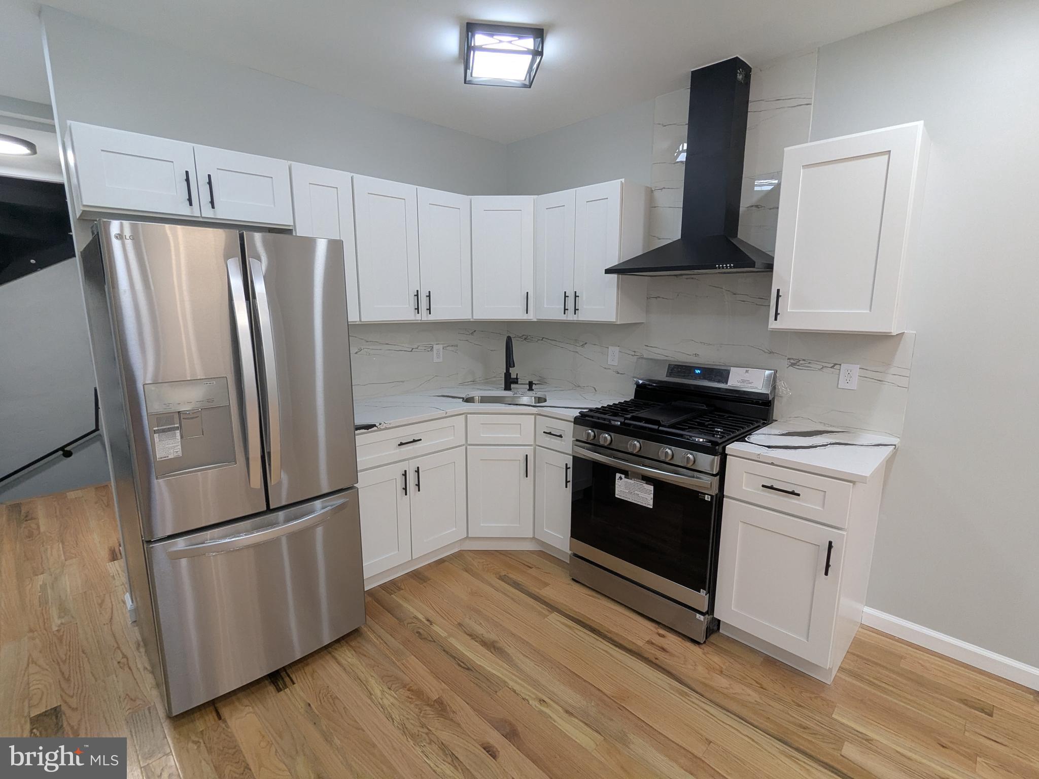 504 North Schroeder Street Baltimore, MD 21223 - Photo 4 of 32 a kitchen with white cabinets stainless steel appliances and wooden floor