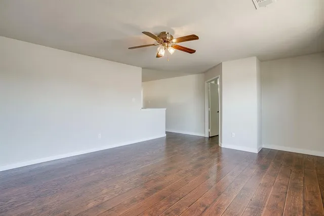 a view of an empty room with wooden floor and a ceiling fan