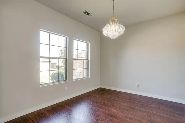 an empty room with wooden floor chandelier and window